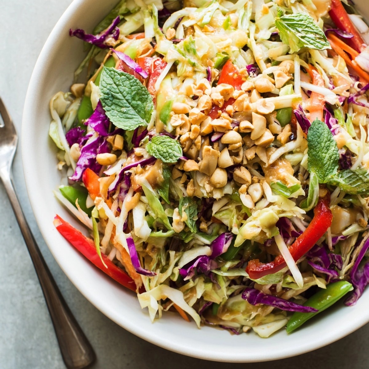 Overhead shot of a vibrant Crunchy Thai Salad Bowl with peanut dressing drizzled.