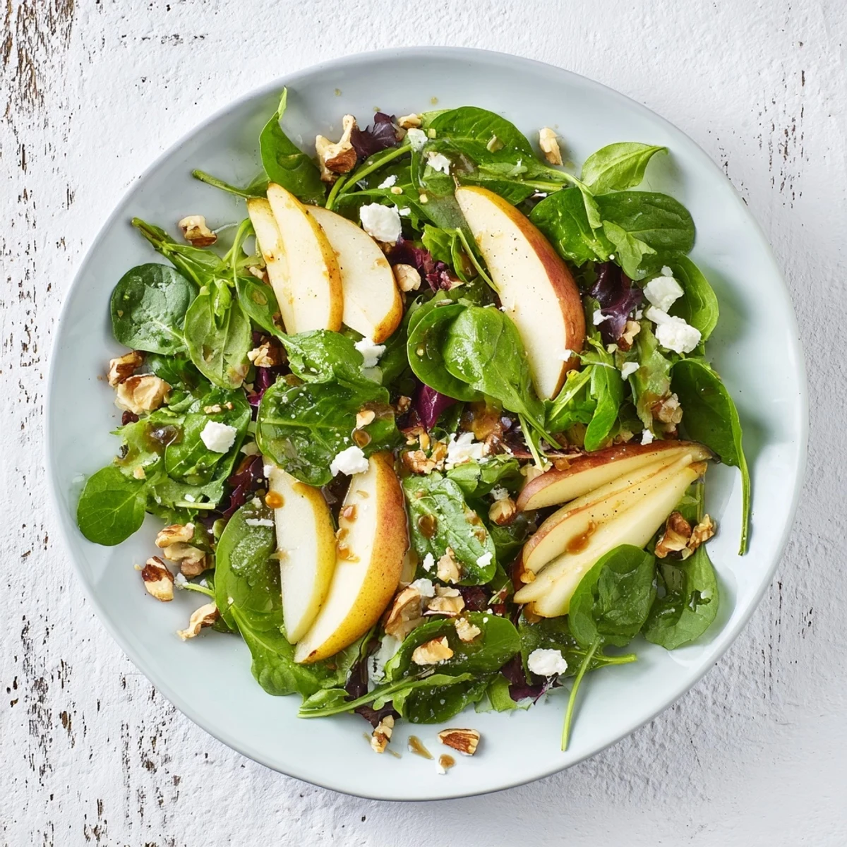 A prepared bowl of Pear & Greens Salad, ready to serve with a light, flavorful dressing and crumbled cheese.