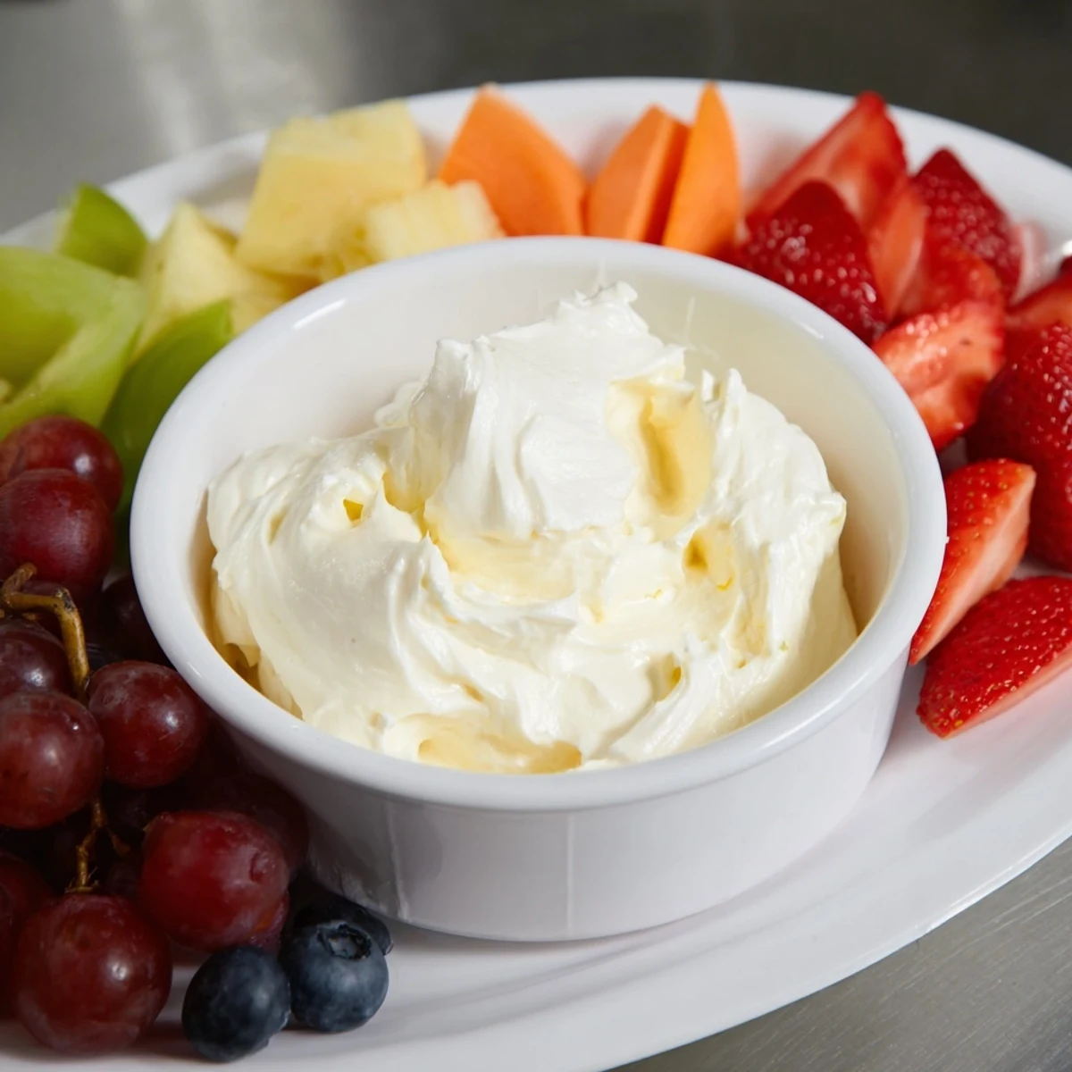 Creamy cream cheese fruit dip in a bowl surrounded by colorful, vibrant fresh berries and melon.