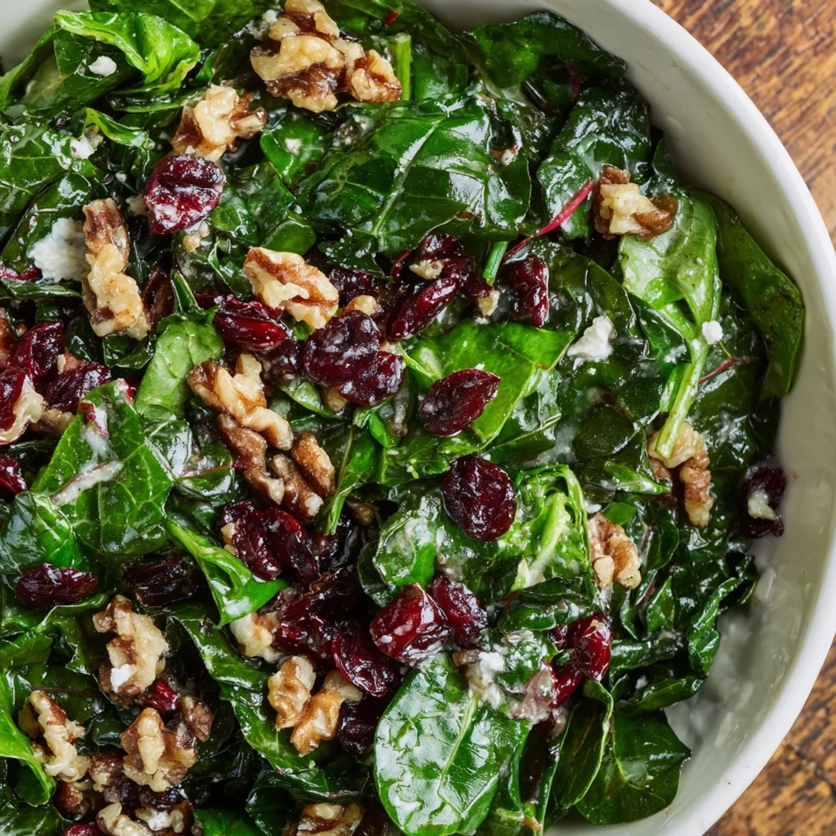 A close-up of Snowy Winter Greens salad topped with creamy goat cheese, crunchy walnuts, and bright dried cranberries.