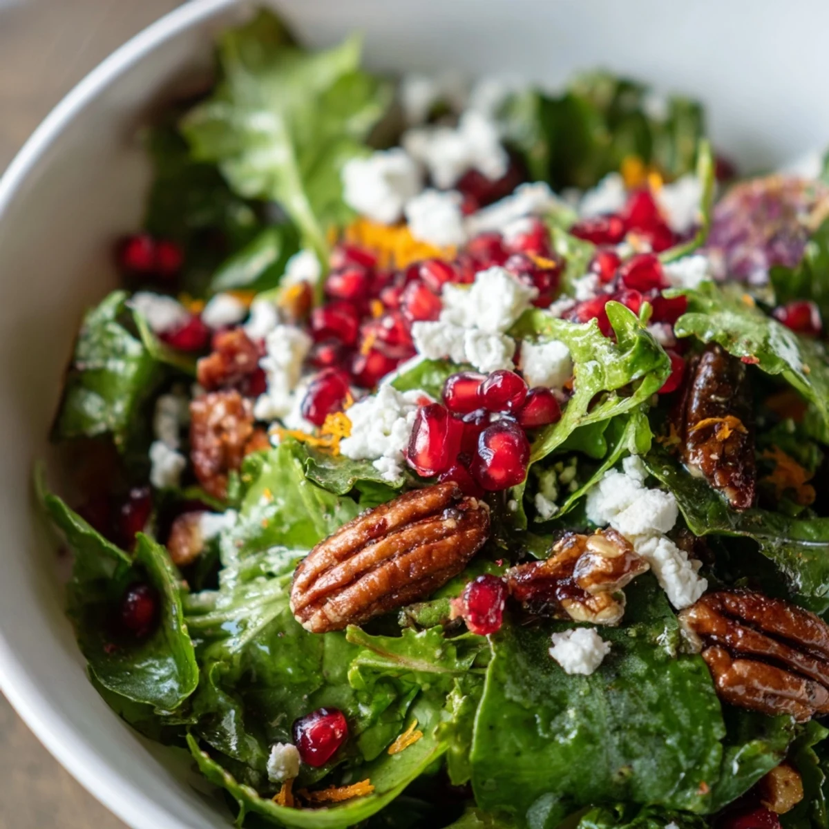 Frosted Winter Greens salad in a white bowl featuring baby greens, pomegranate seeds, and a frosty citrus dressing.