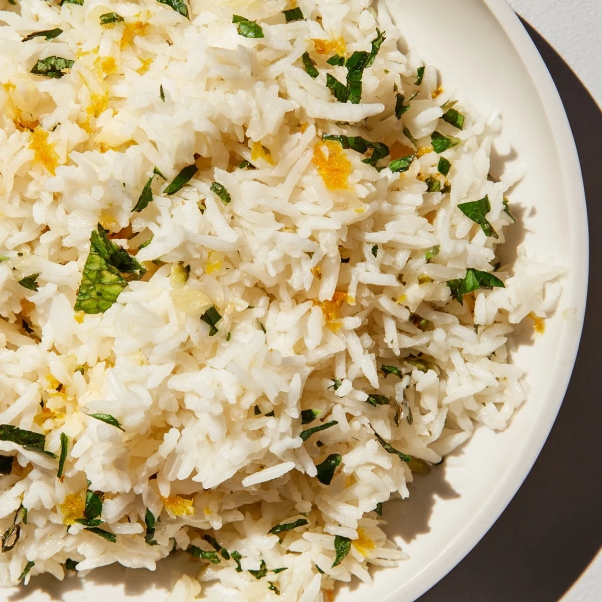 Warm Citrus Rice garnished with fresh parsley and mint, vibrant orange and lemon zest, in a white bowl.