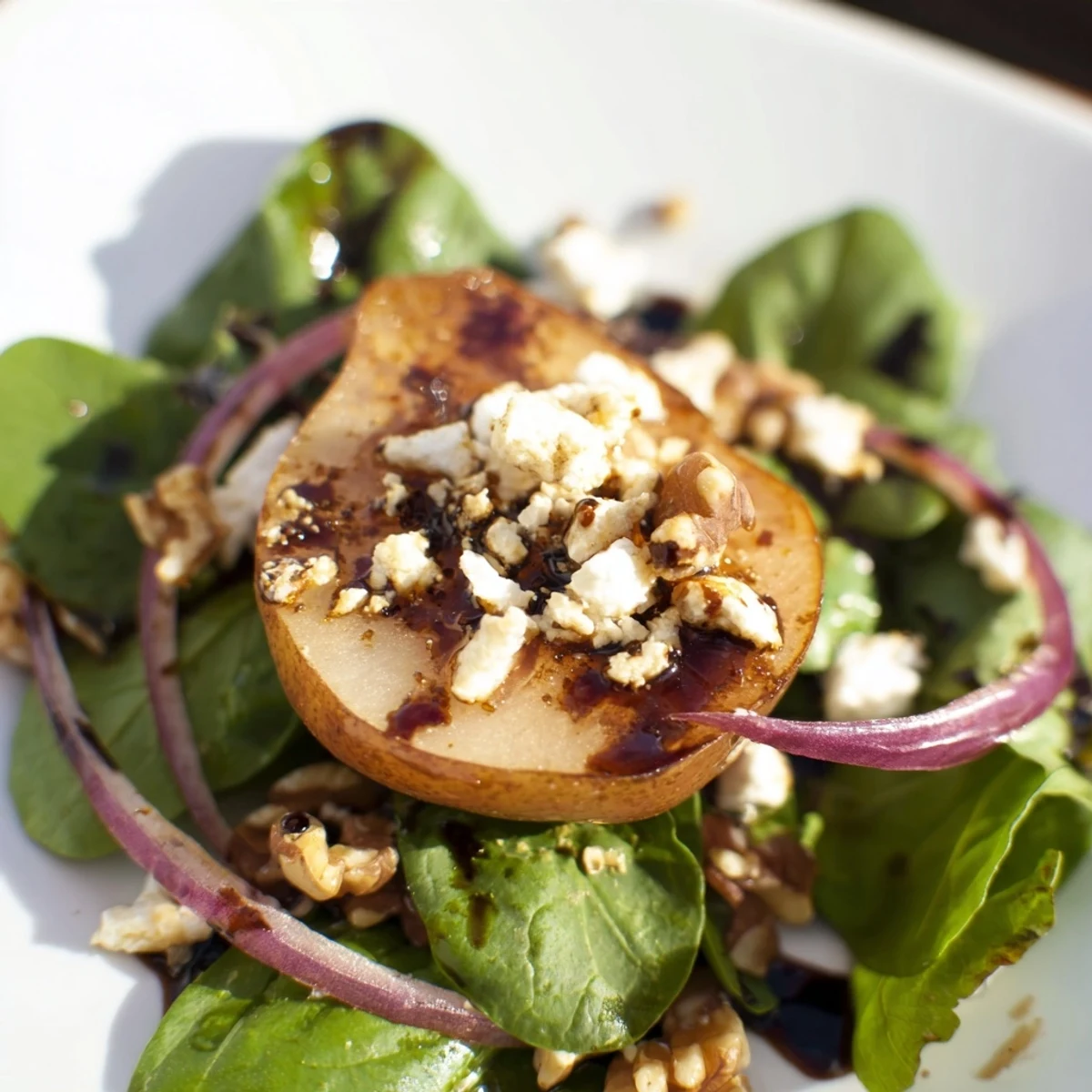 A freshly tossed Warm Pear Greens salad drizzled with tangy vinaigrette, garnished with toasted nuts and red onion slices.