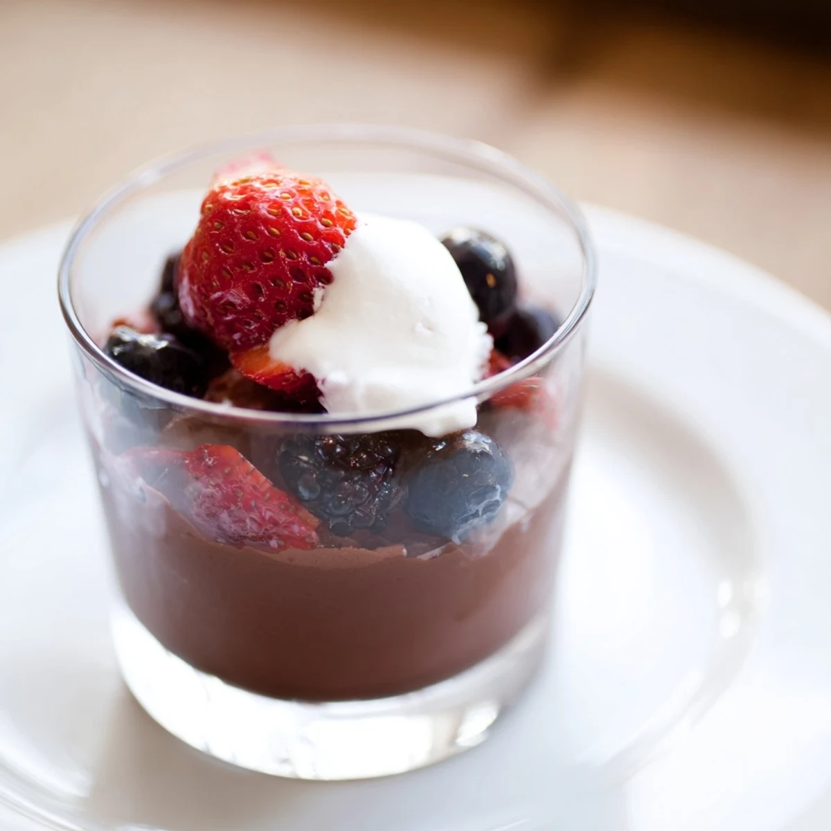 Rich Frosted Cocoa Berry plated with fresh strawberries and raspberries, a glossy chocolate mousse, and a cool dollop of vanilla whipped cream.