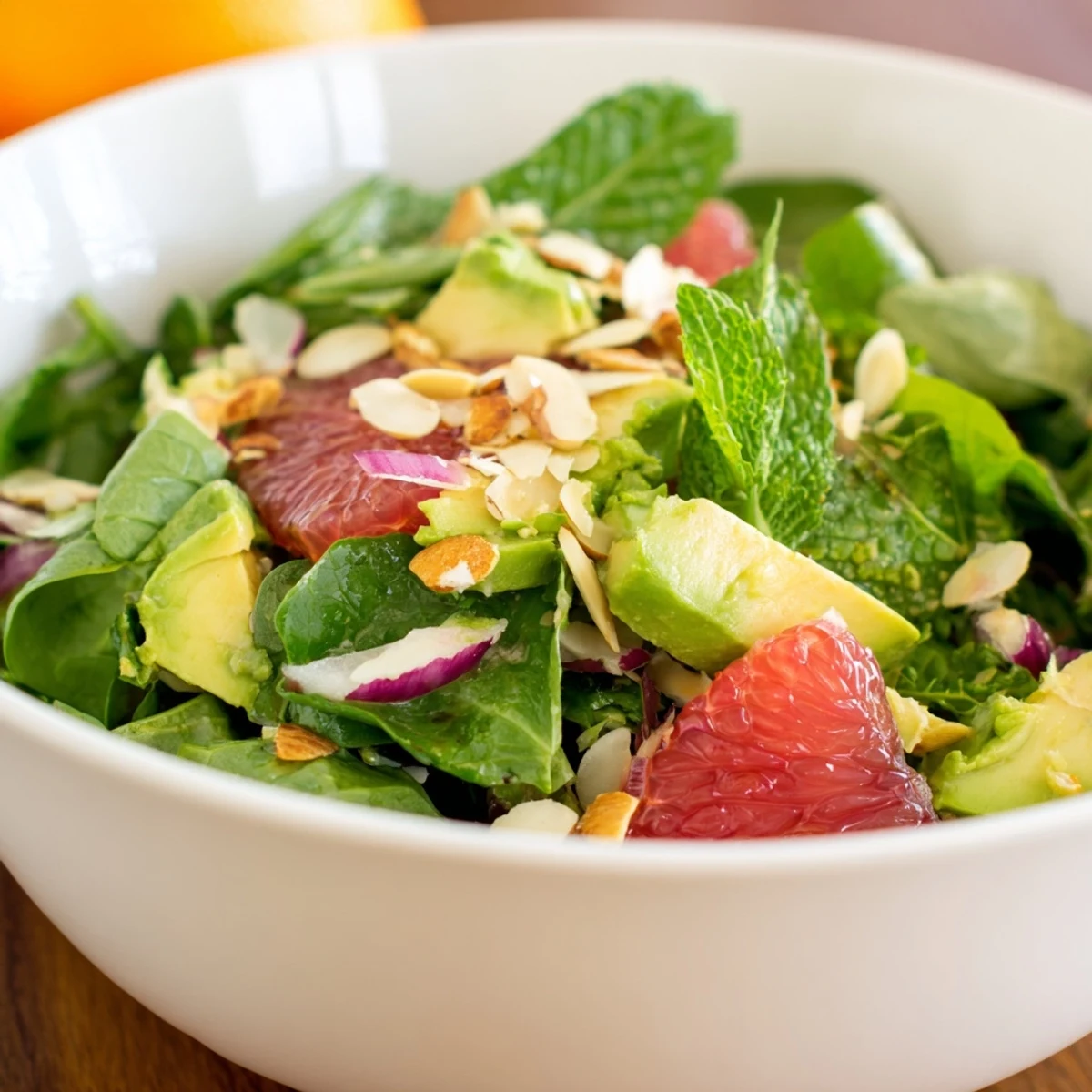 A bowl of Evergreen Citrus Greens topped with creamy avocado, sliced red onion, and mint.