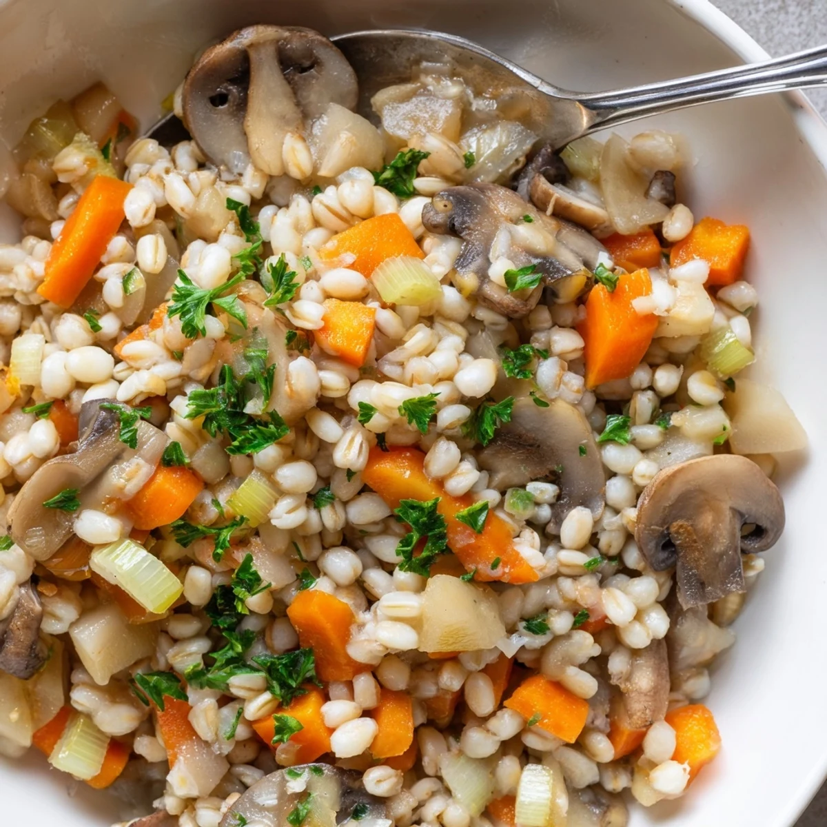 Freshly cooked Hearth Barley in a white bowl, featuring mushrooms and carrots in a savory herb broth.