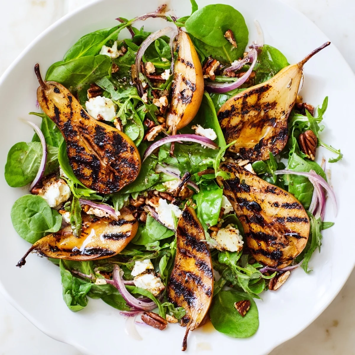 Golden, charred pear slices arranged over fresh greens, red onion, and nuts on a rustic white platter.
