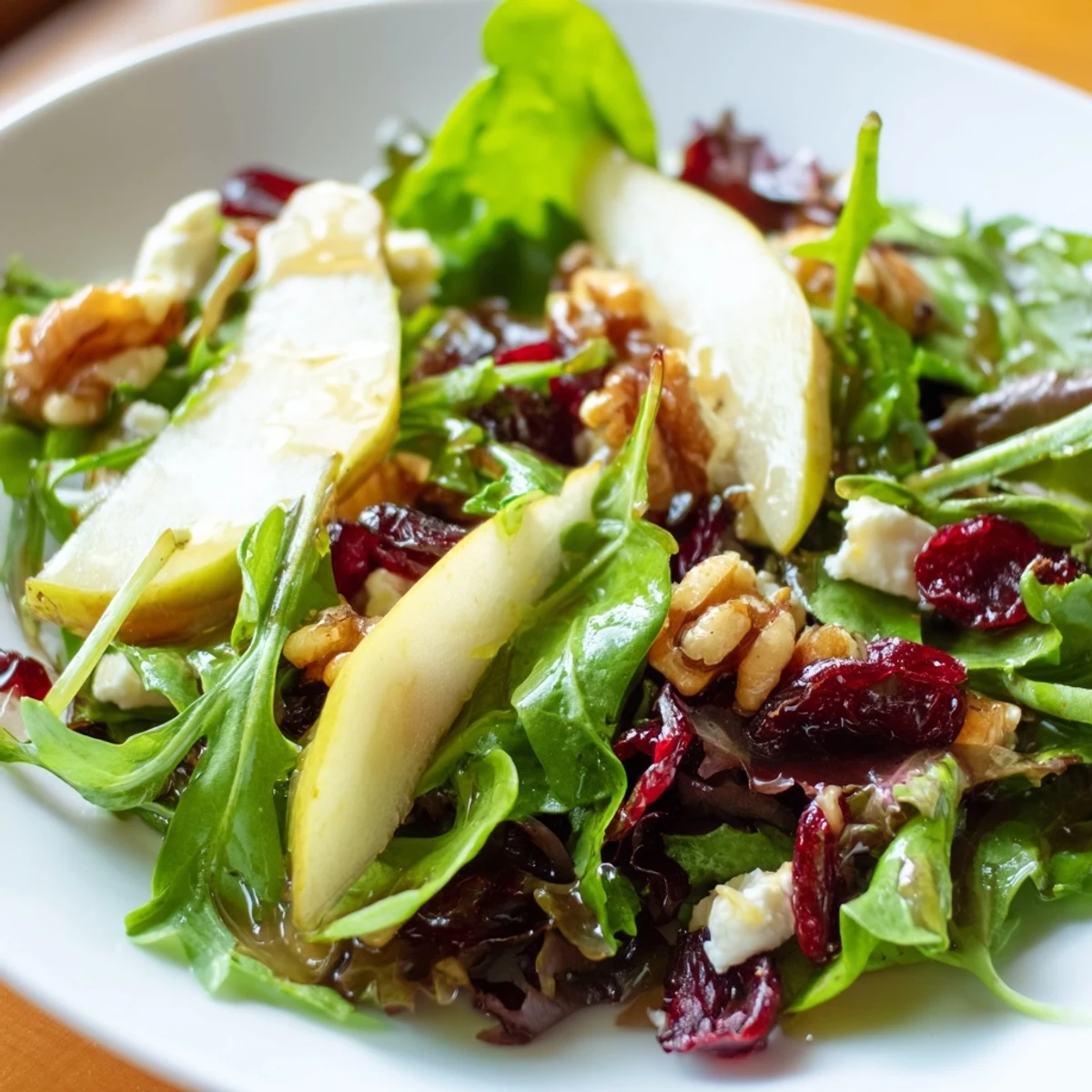 Plated Cranberry Pear Greens salad with tender greens, ripe pear wedges, dried cranberries, walnuts, and goat cheese, ready to serve.