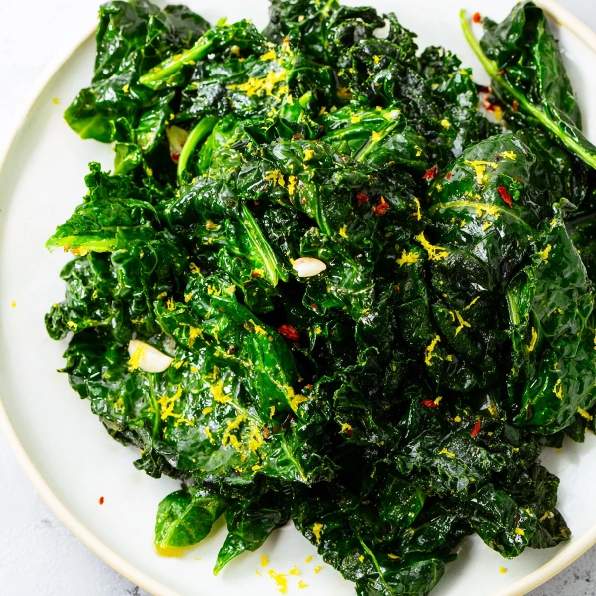 A close-up of vibrant Emerald Winter Greens sautéed with garlic, garnished with fresh lemon zest and red pepper flakes, served as a healthy vegan side.