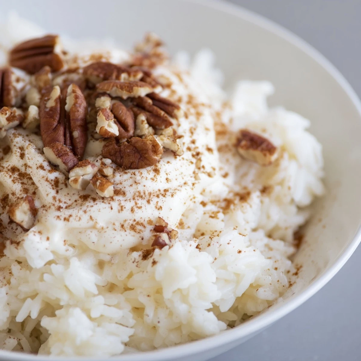 A comforting serving of Frosted Warm Rice topped with rich cream cheese frosting and chopped walnuts, ready to enjoy.