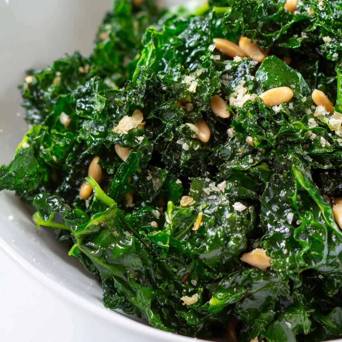 A close-up view of vibrant green Cozy Kale, topped with crunchy toasted pine nuts and a sprinkle of Parmesan cheese.  