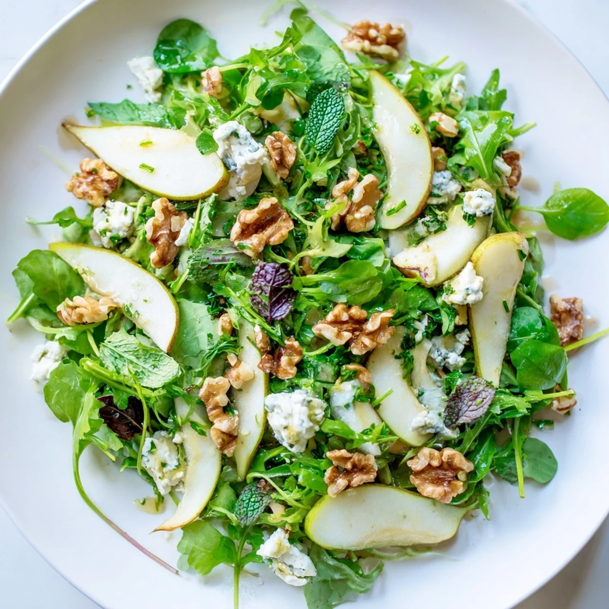 Freshly sliced pears and tender greens tossed with mint and parsley in a light vinaigrette, ready to serve.