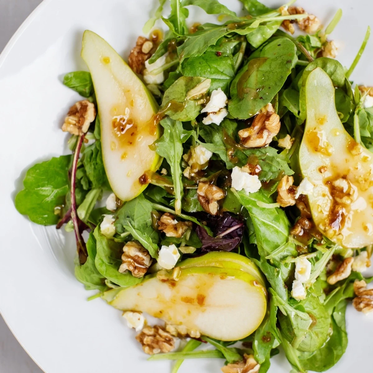 Bright bowl of Evergreen Pear Greens, featuring tender arugula and spinach topped with pear slices and crunchy walnuts, perfect as a light side.