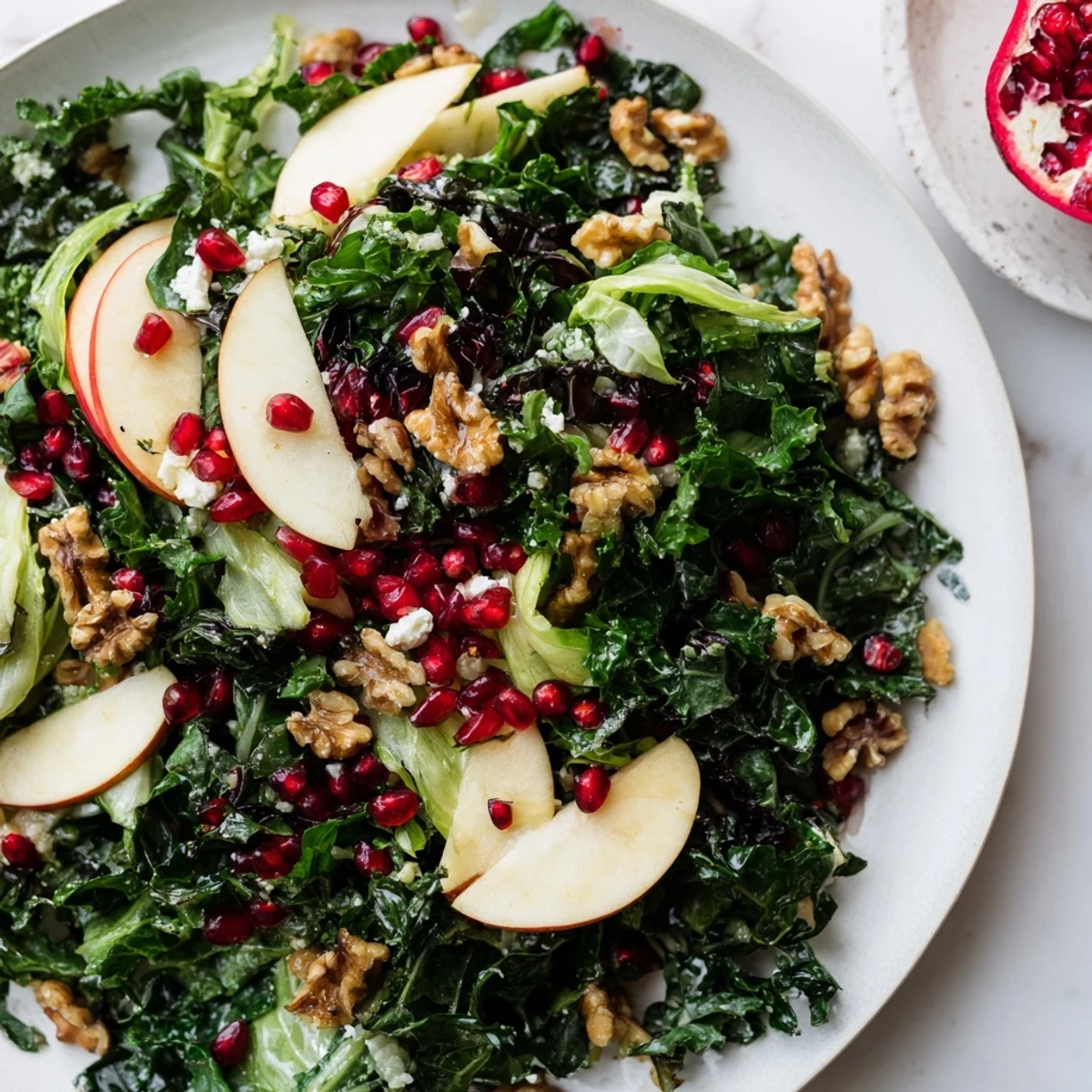 A close-up of Winter Greens Salad with kale, Swiss chard, spinach, apple slices, pomegranate seeds, toasted walnuts, and crumbled goat cheese.