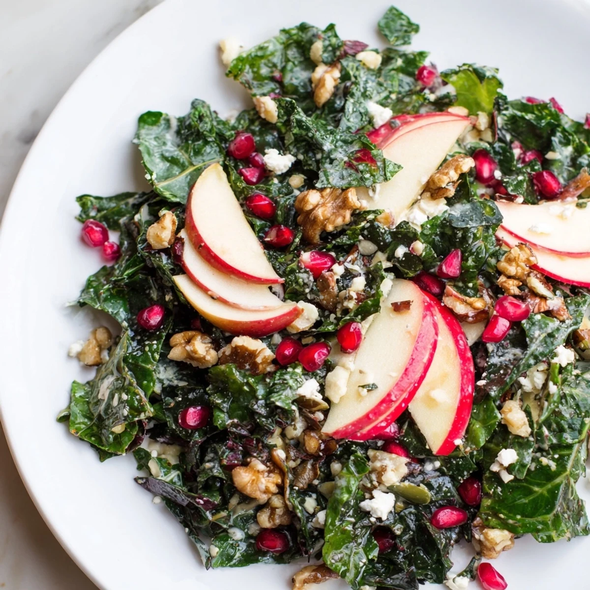 Overhead view of Winter Greens Salad on a rustic plate, tossed with apple cider vinaigrette and garnished with chopped walnuts and pomegranate seeds.