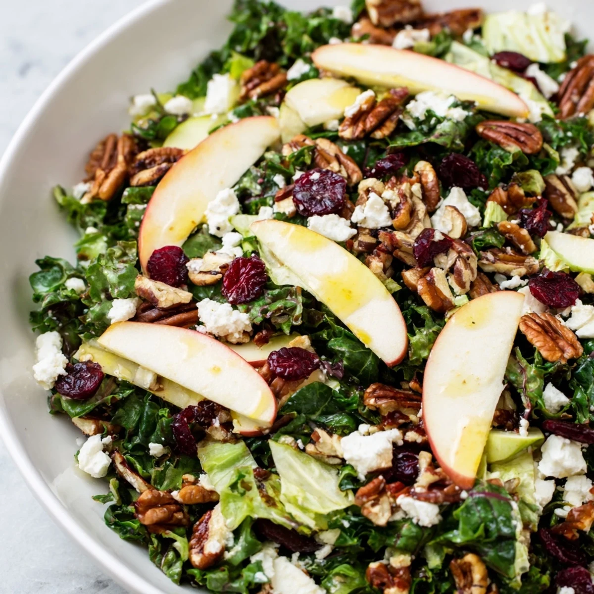 Fresh Harvest Winter Greens salad topped with sliced apple, cranberries, pepitas, and creamy crumbled goat cheese on a rustic wooden table.