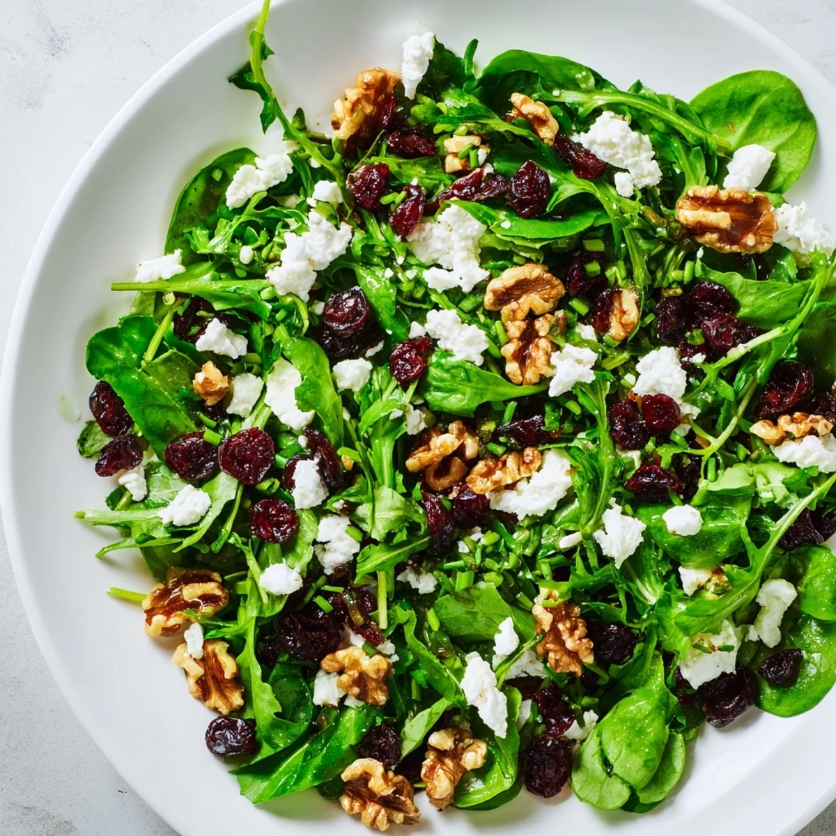 Emerald Cranberry Herb salad features bright greens, dried cranberries, and crumbled goat cheese on a rustic plate.