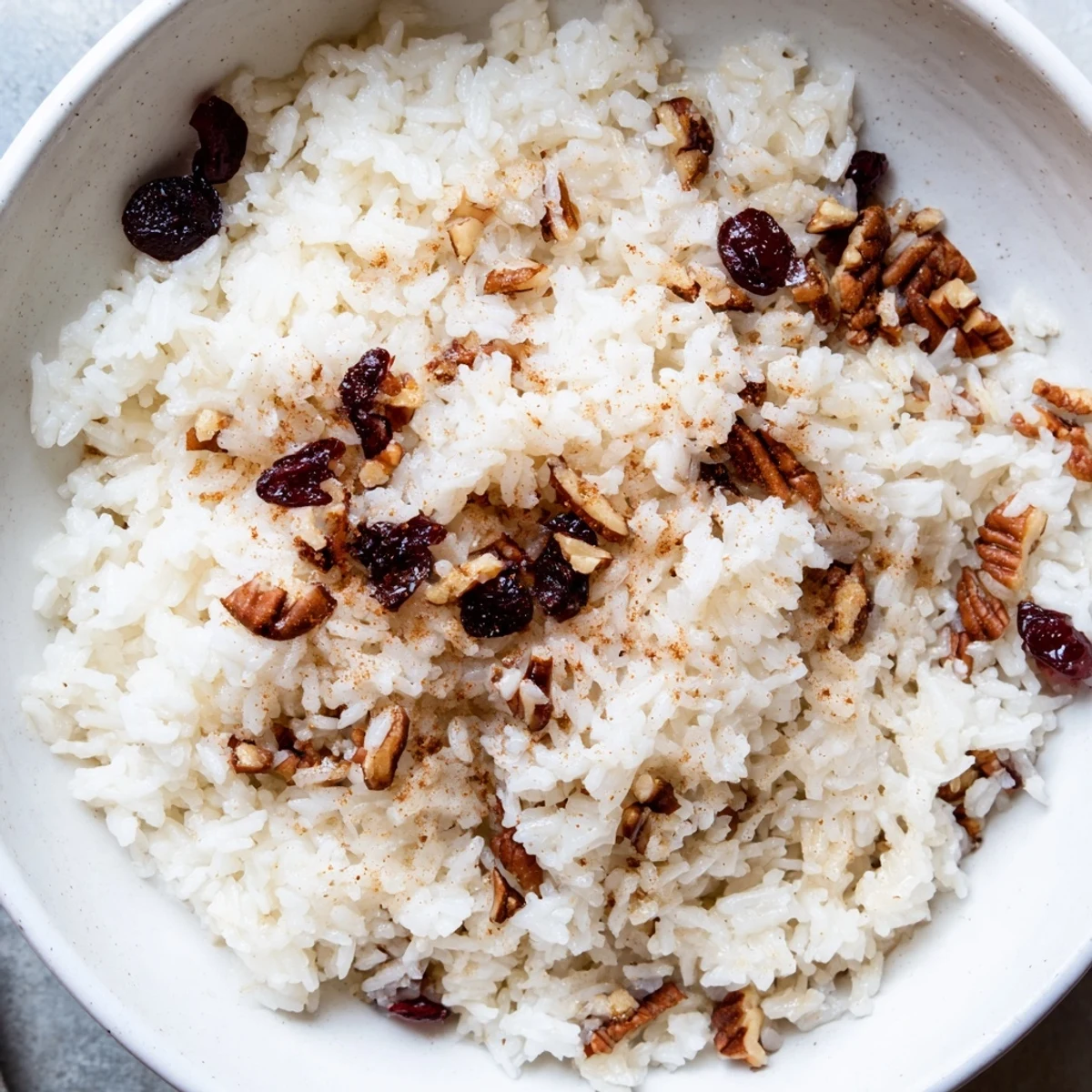 A close-up of Maple Warm Rice in a white bowl, topped with toasted pecans and dried cranberries. The fluffy grains glisten with a light maple glaze, promising a sweet and cozy comfort.