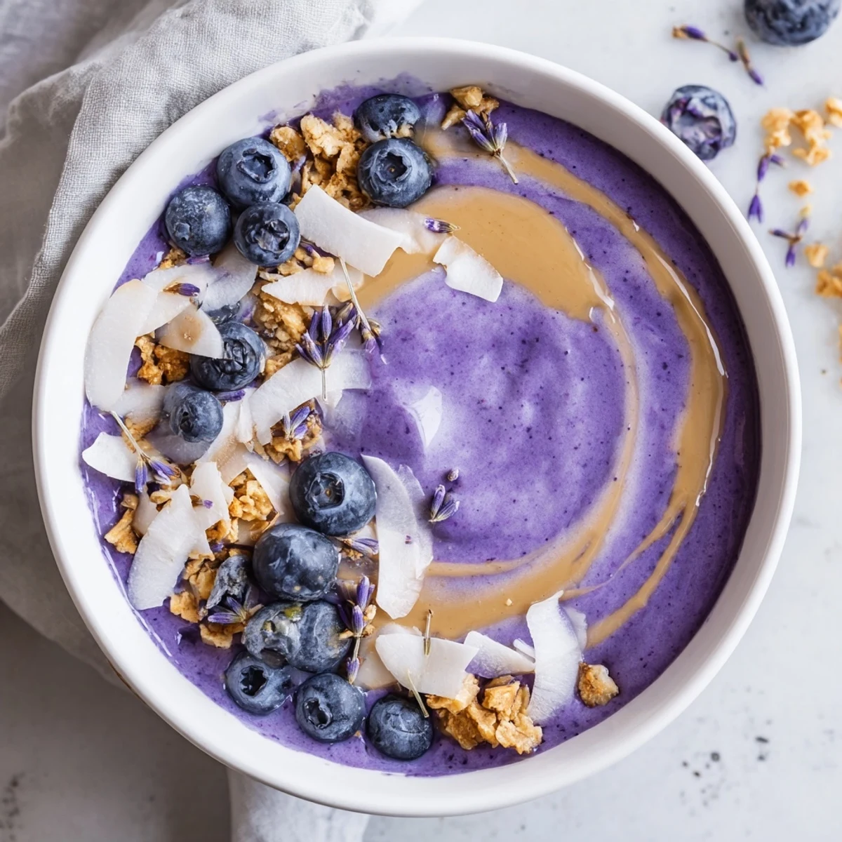 A vibrant Blueberry Lavender Smoothie Bowl with Almond Butter Swirl topped with fresh berries and crunchy granola.