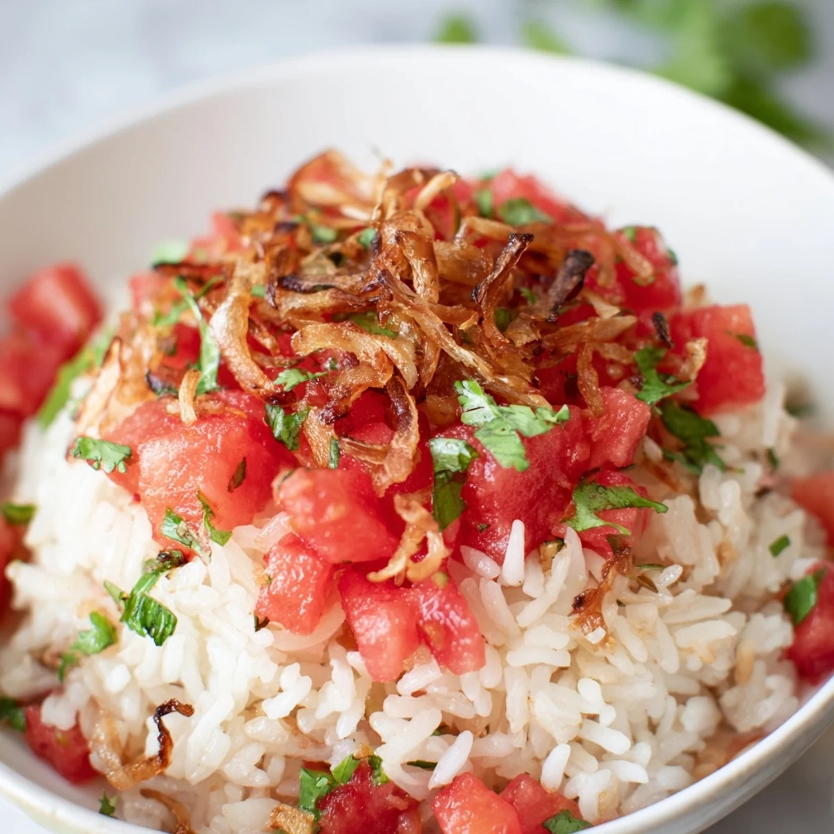 A bowl of Chili Lime Watermelon Rice Dish with Crispy Shallots showing fluffy grains mixed with bright red watermelon cubes, fresh cilantro, and crunchy golden toppings.