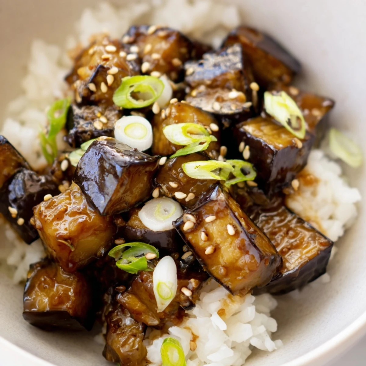 A close-up of Miso Glazed Eggplant Rice Dish with Scallions, showing tender eggplant cubes glistening with dark miso glaze atop fluffy white rice.