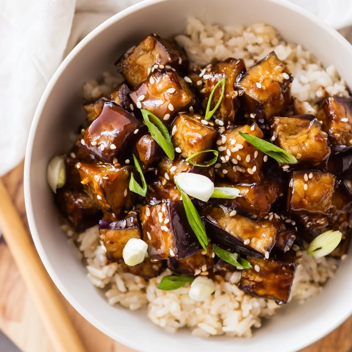 The Miso Glazed Eggplant Rice Dish with Scallions is served in a ceramic bowl, garnished with fresh green onions and toasted sesame seeds.