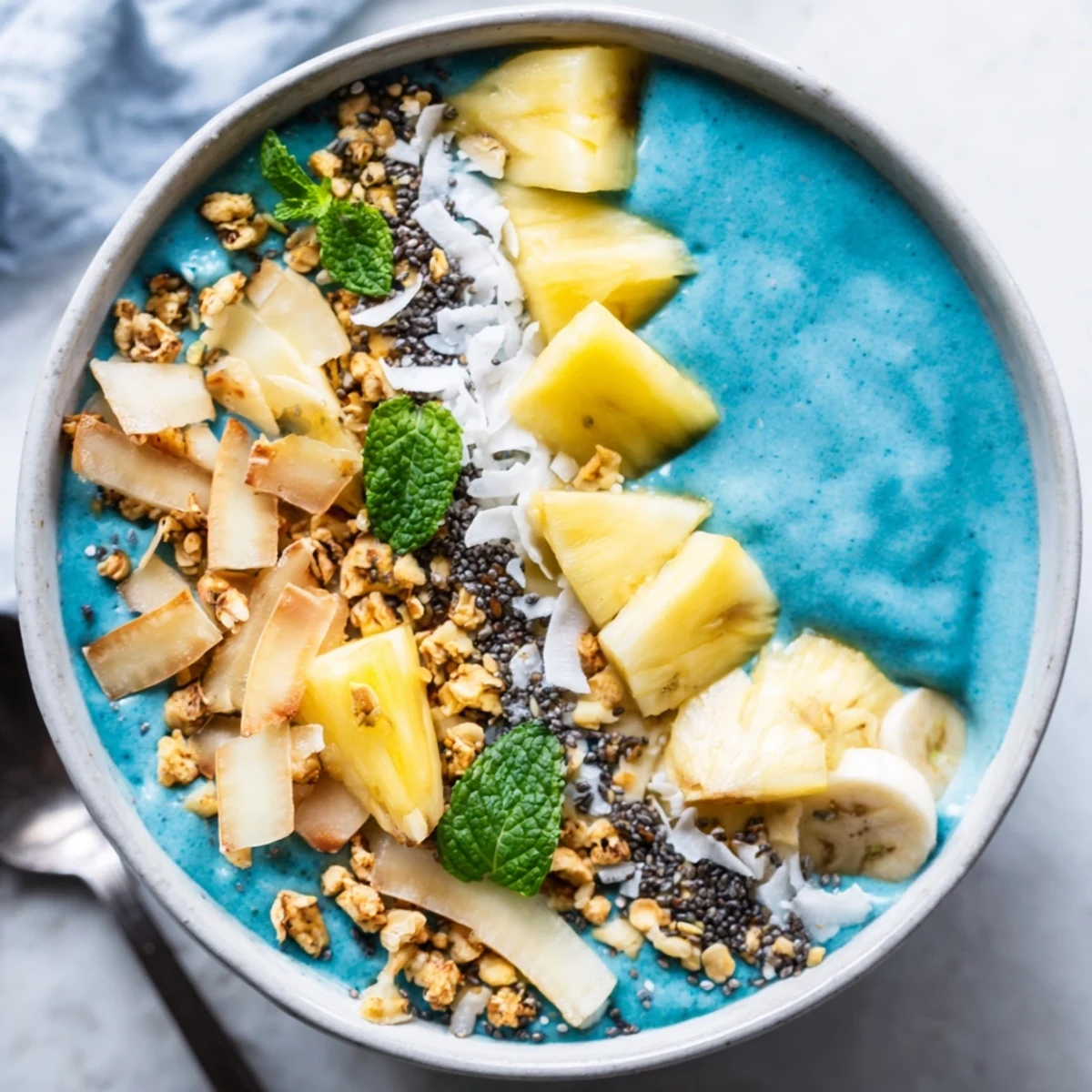Creamy blue spirulina pineapple smoothie bowl served with toasted coconut, fresh fruit, and chia seeds.