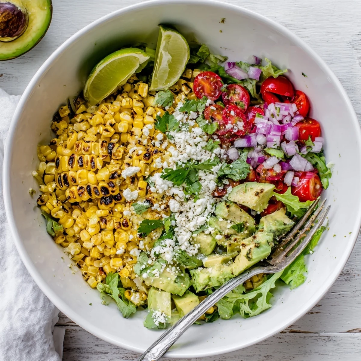 Vibrant lime dressing coats this Charred Corn and Avocado Salad Bowl, served over greens with a garnish of cilantro for a zesty summer side.