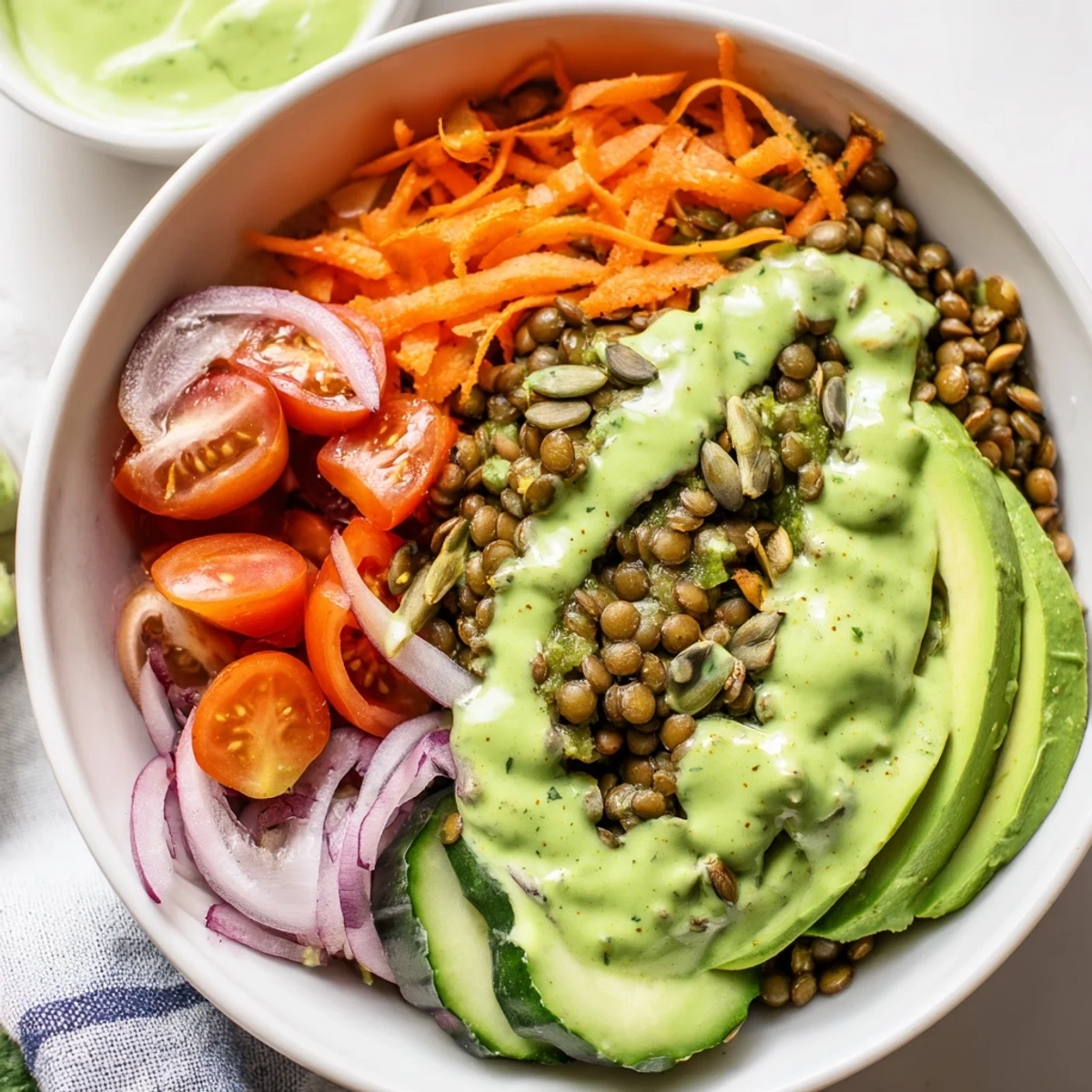 Colorful Green Goddess Lentil Vegan Bowl with Pickled Onions served over mixed greens and ripe cherry tomatoes.
