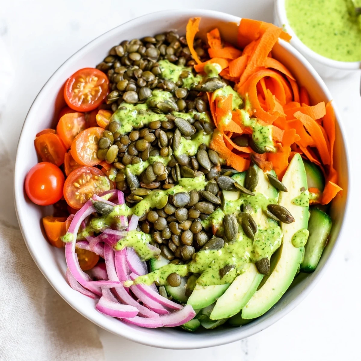 Freshly prepared Green Goddess Lentil Vegan Bowl with Pickled Onions featuring crunchy cucumbers and toasted pumpkin seeds.
