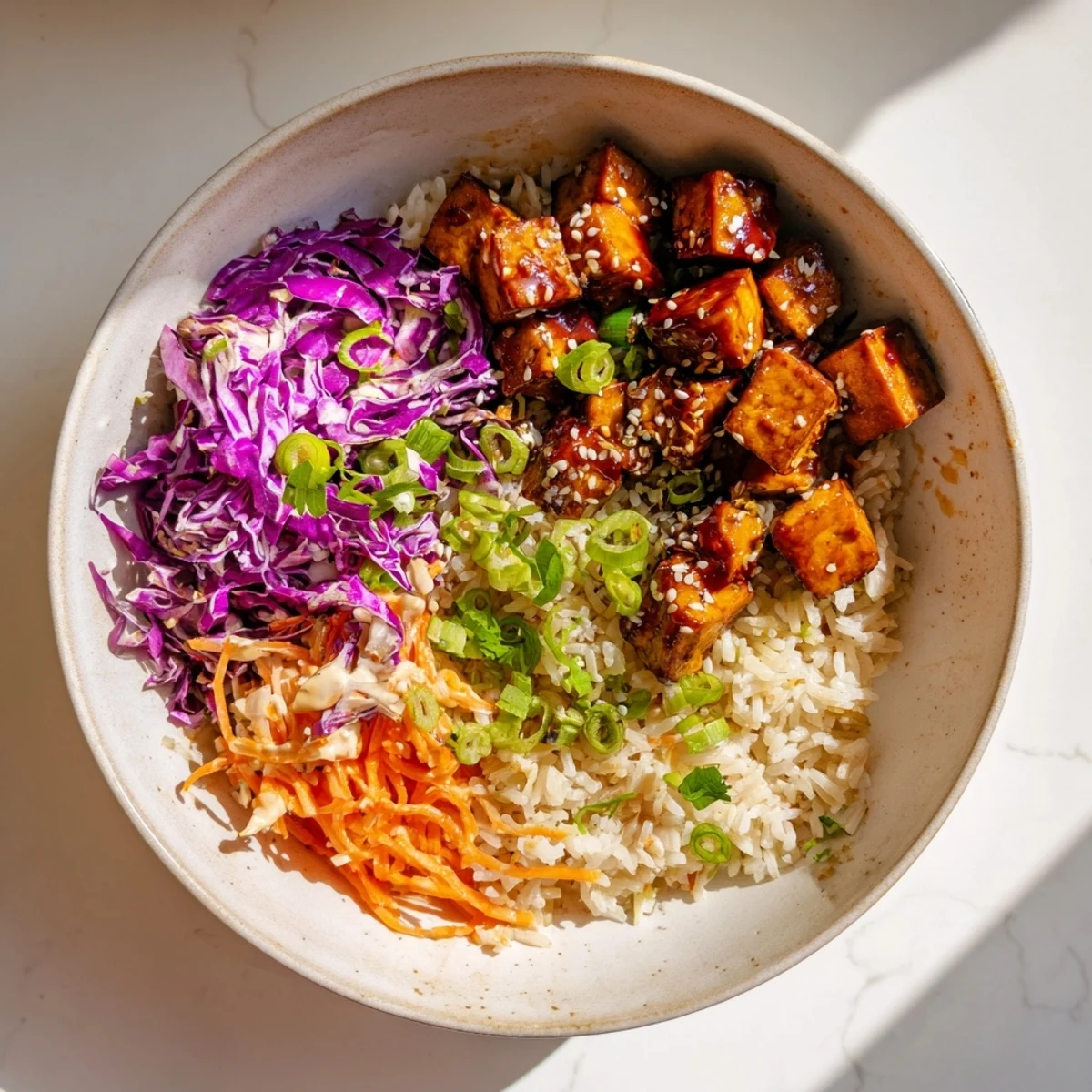 Crispy tofu cubes coated in a sticky sriracha maple glaze sit atop fluffy jasmine rice with a colorful sesame slaw in this vegan bowl.