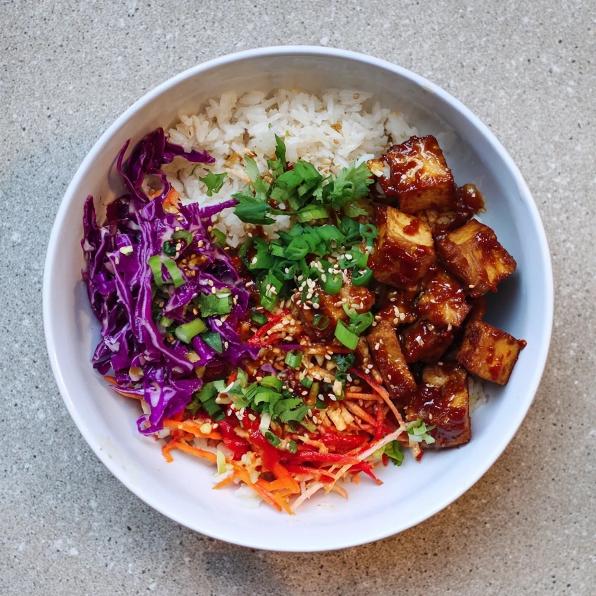 Golden tofu with spicy sriracha maple glaze nestled in a bowl of rice and vibrant sesame slaw, ready to eat.