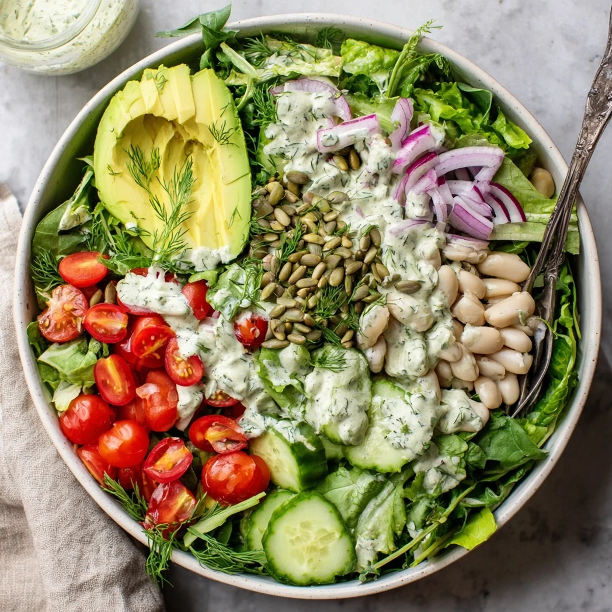 Freshly prepared Creamy Dill Pickle Salad Bowl with hearty white beans and avocado, served on a light bed of greens.