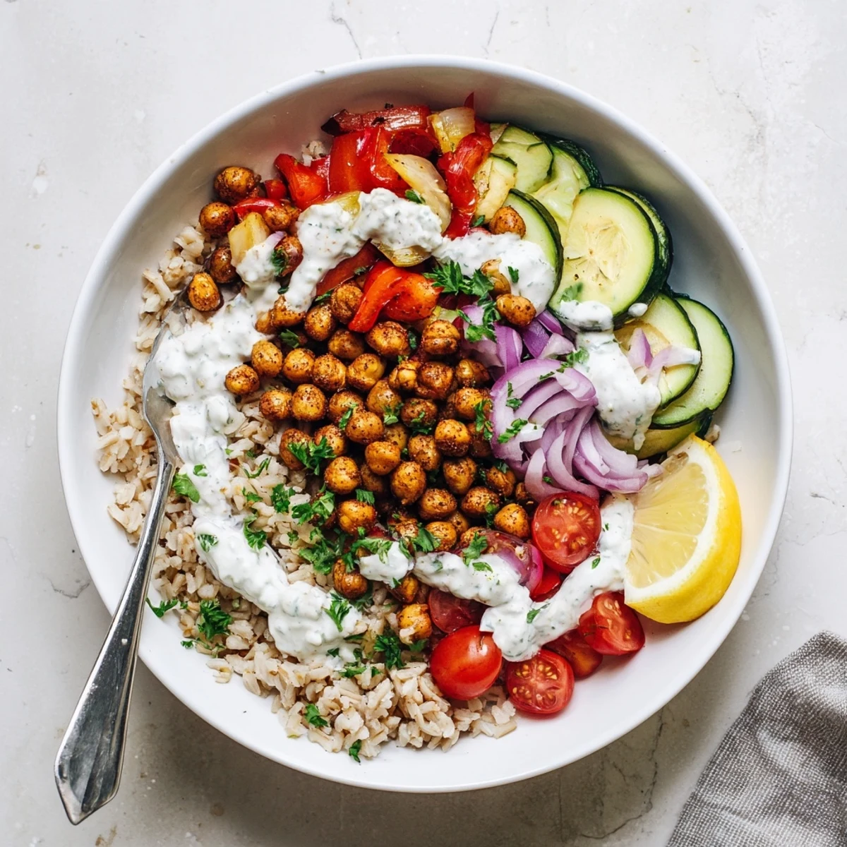 Overhead view of Smoky Paprika Chickpea Veggie Bowl with Lemon Yogurt, served on quinoa with parsley garnish and lemon wedges.