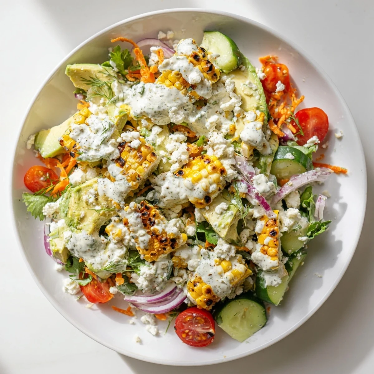 Close-up of Creamy Avocado Ranch Salad Bowl with Grilled Corn, drizzled with homemade ranch dressing, tomatoes, cucumbers, and red onion.