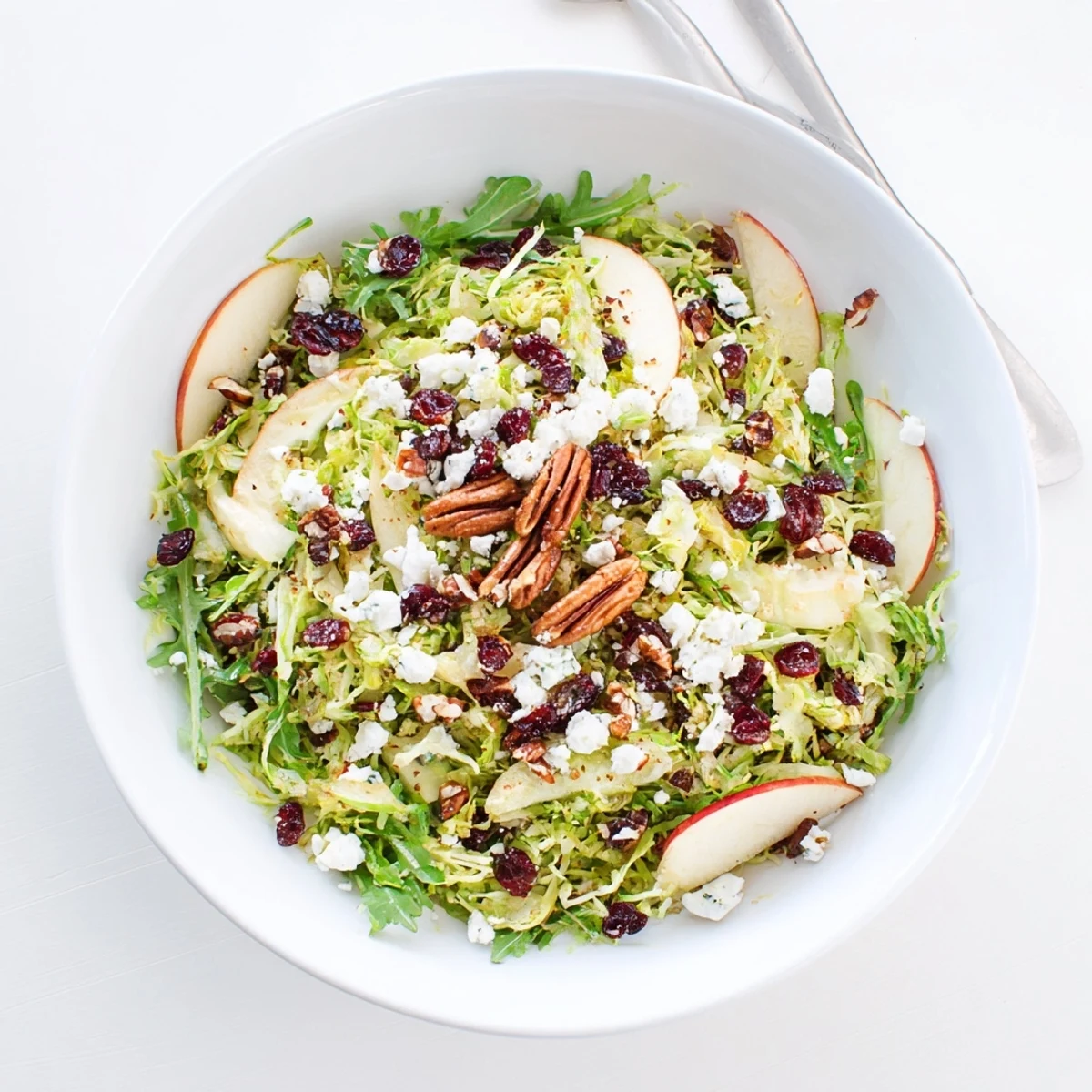 Close-up of a Shaved Brussels Sprout and Apple Salad Bowl with Candied Pecans showing crisp greens and sweet crunchy toppings.