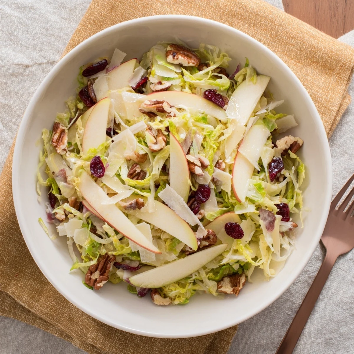 Shaved Brussels Sprout and Apple Salad Bowl with Candied Pecans garnished with red onion and dried cranberries.