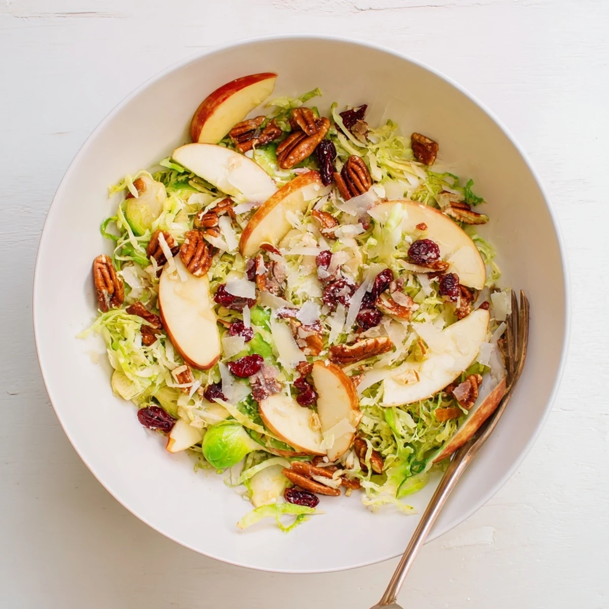 Fresh, vegetarian salad bowl featuring shaved Brussels sprouts, sliced apples, and candied pecans ready to serve.