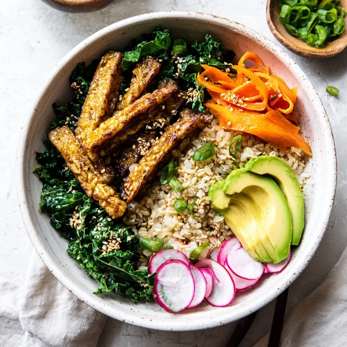 Sliced avocado, julienned carrots, and scallions garnish a vibrant Maple Miso Tempeh Vegan Bowl with sesame greens. 