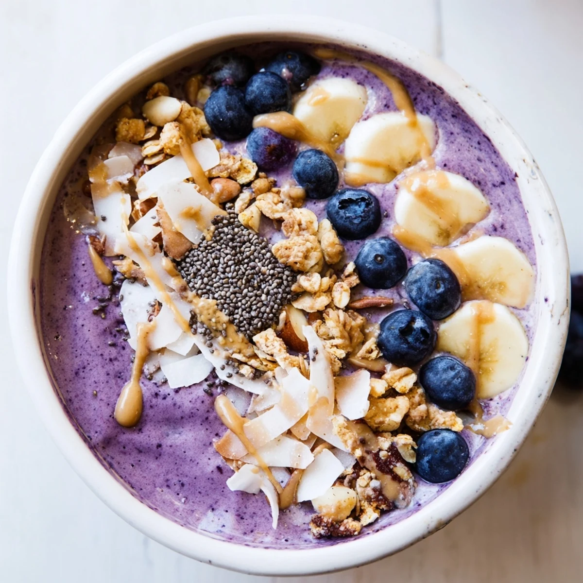 A vibrant Blueberry Almond Butter Smoothie Bowl with Chia Crunch topped with fresh banana slices and a drizzle of almond butter.