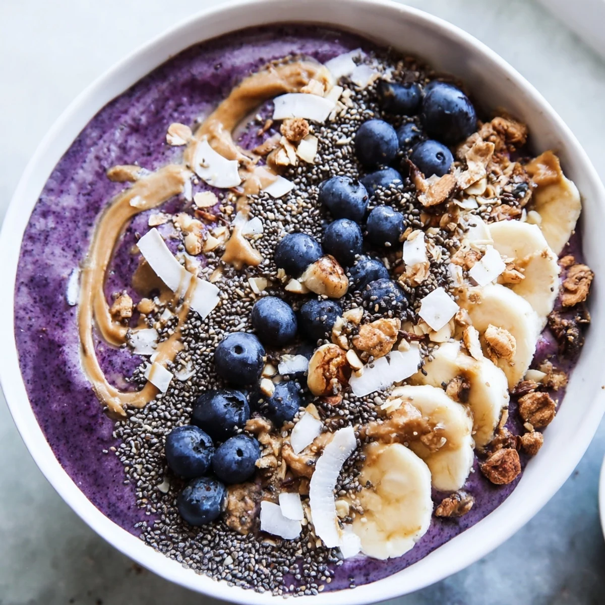 The creamy Blueberry Almond Butter Smoothie Bowl with Chia Crunch is garnished with sliced almonds and coconut for a delightful breakfast.