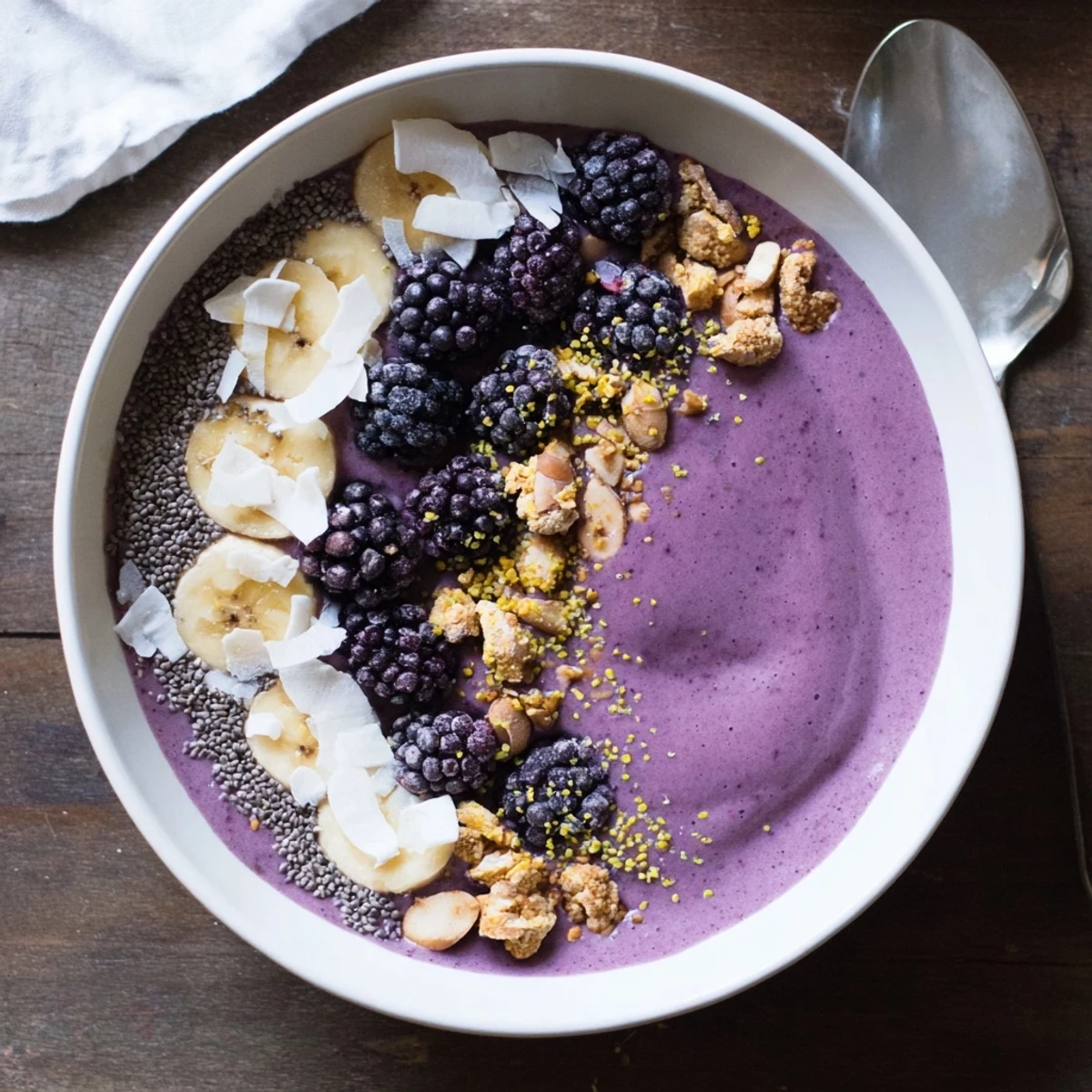 Creamy blackberry smoothie bowl in a white ceramic bowl arranged with banana slices, coconut flakes, and chia seeds