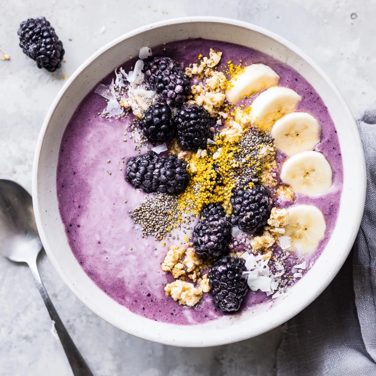 Vibrant purple smoothie bowl featuring cashew base topped artfully with fresh blackberries and a sprinkle of bee pollen