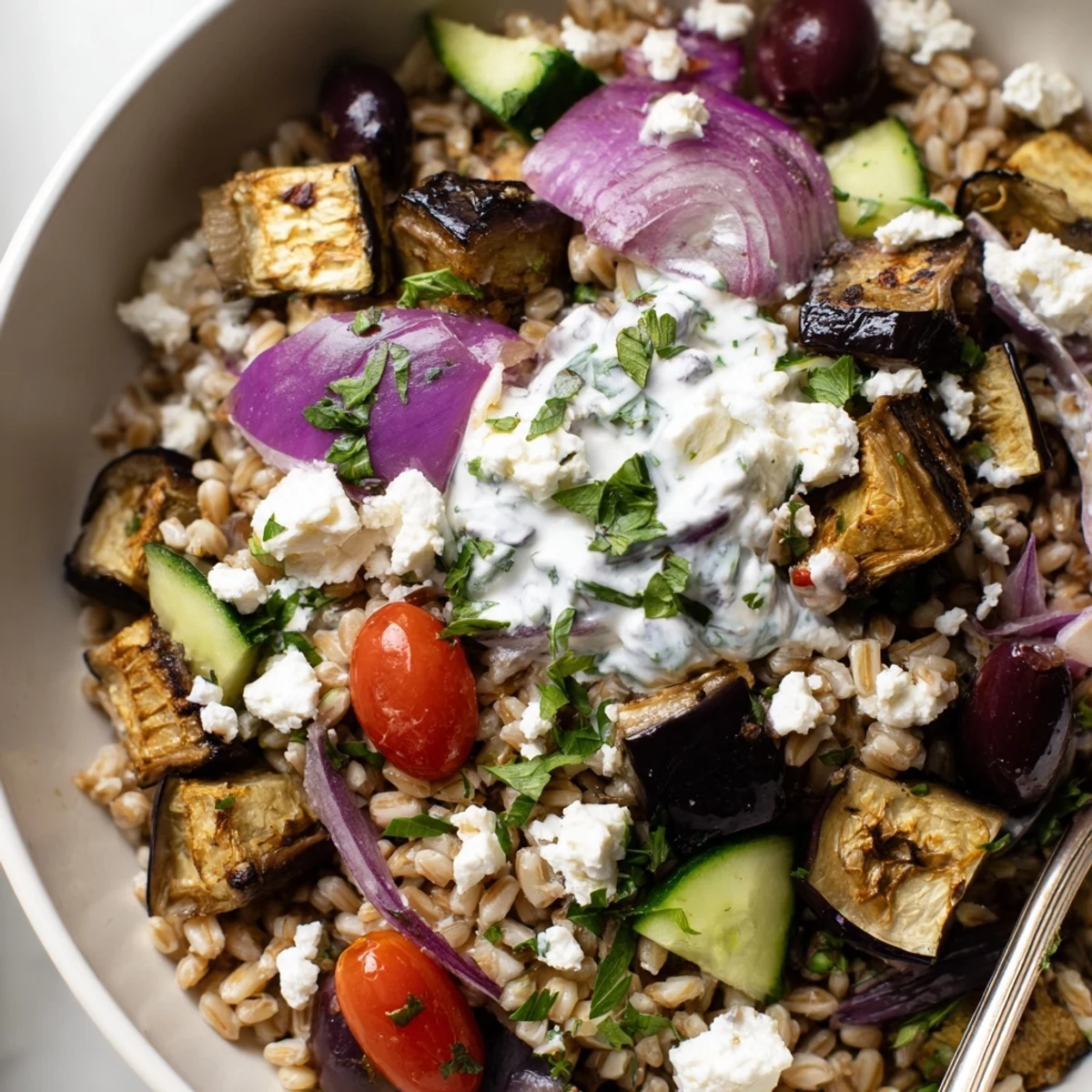 Colorful Mediterranean roasted eggplant grain bowl topped with fresh vegetables and creamy tzatziki sauce