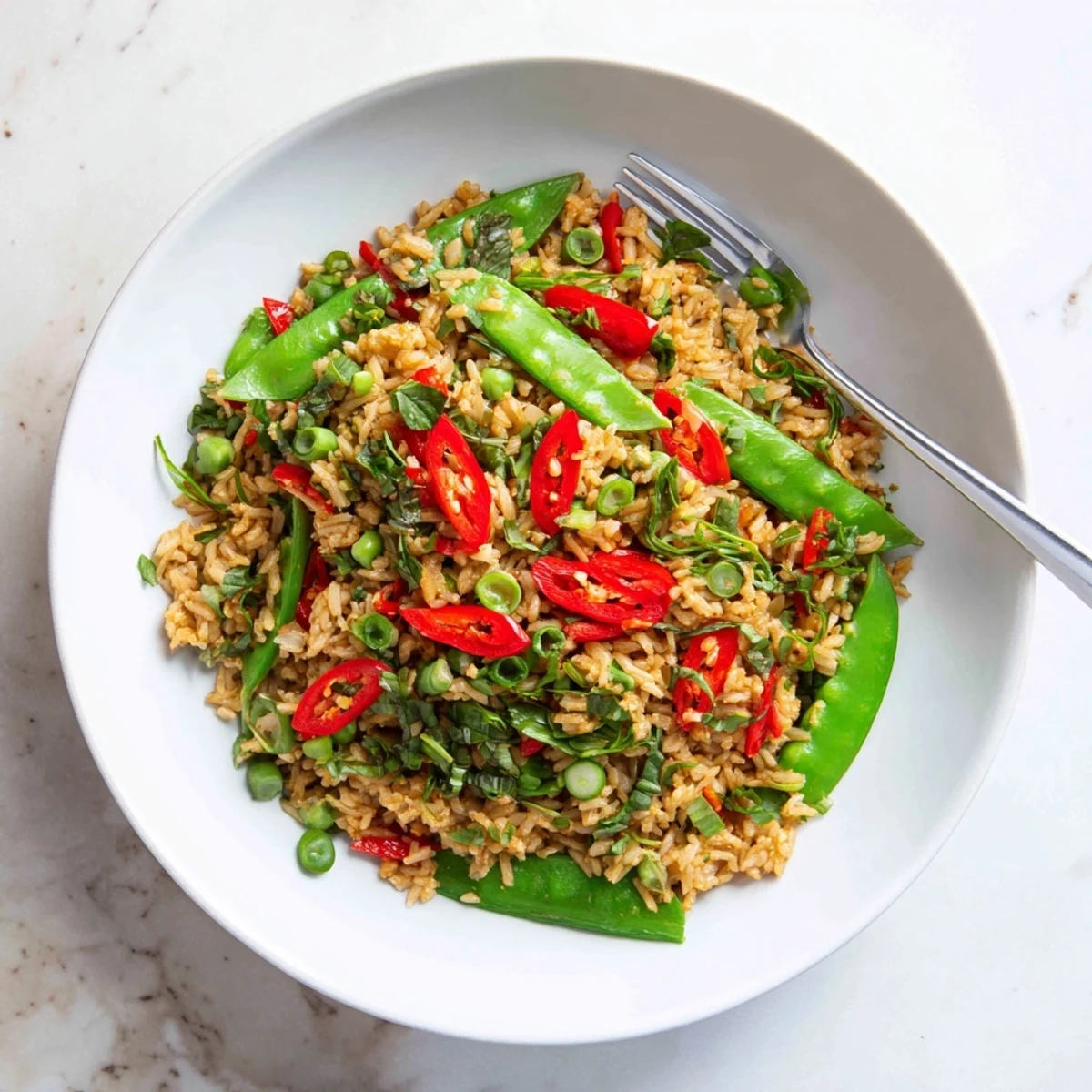 Golden Thai basil garlic fried rice with crisp snap peas in a white bowl