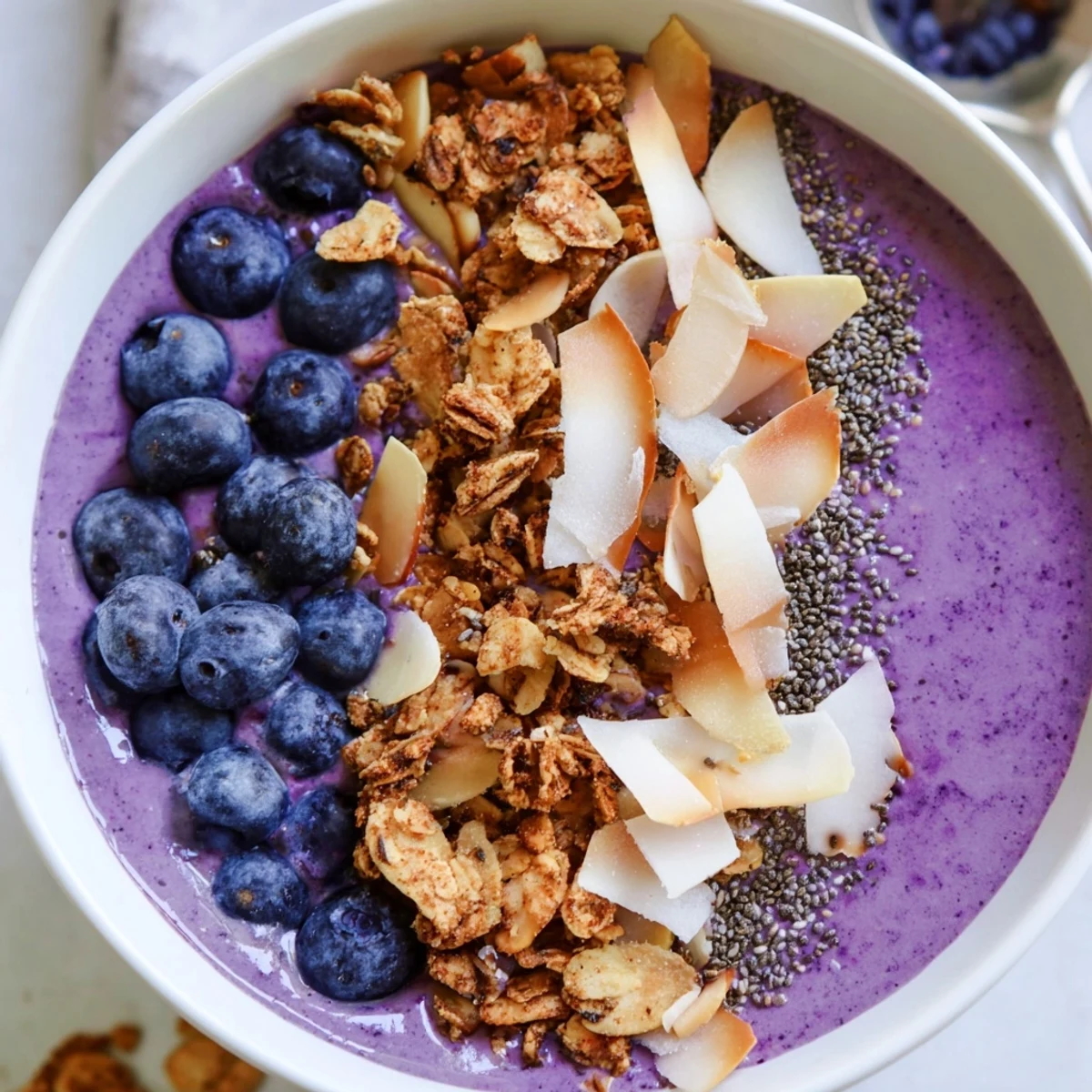 Thick purple smoothie bowl with creamy coconut base, almonds, and coconut flakes