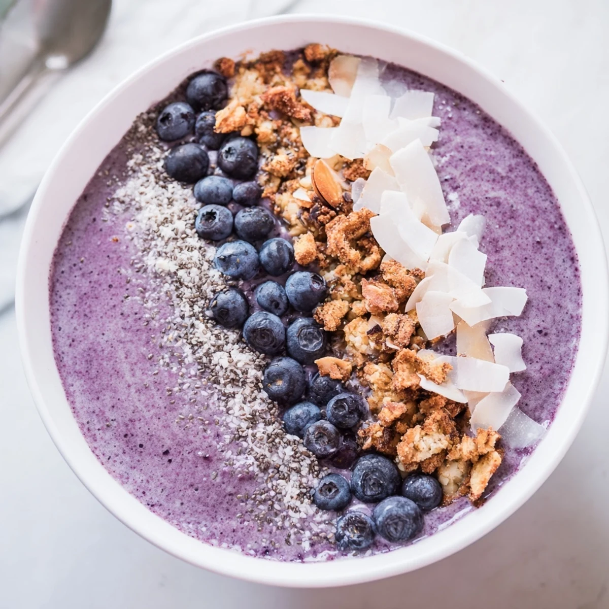 Colorful breakfast smoothie bowl featuring blueberry blend with granola crumble and sliced almonds