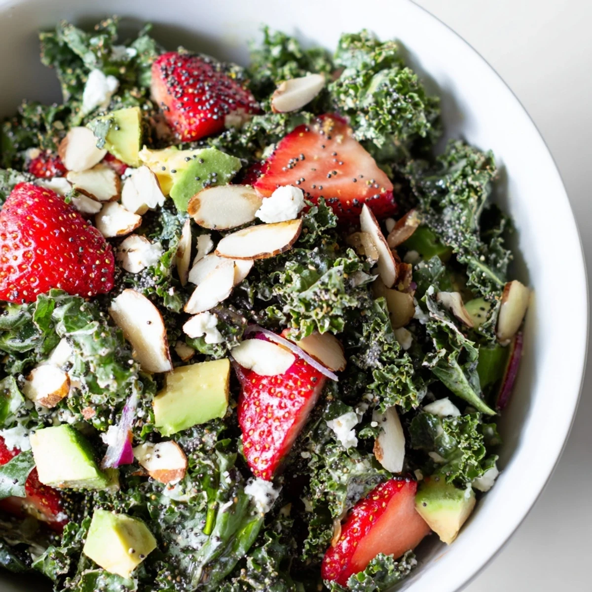 Fresh kale salad topped with juicy strawberries and creamy goat cheese in sweet poppyseed dressing