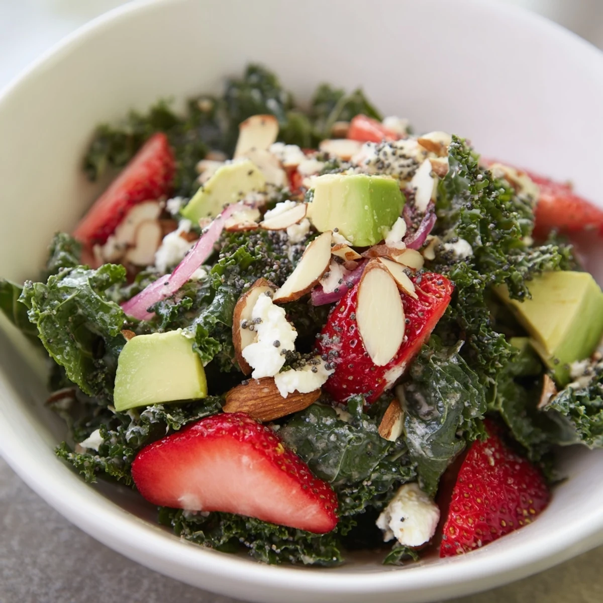 Vibrant salad bowl featuring massaged kale, sliced strawberries, almonds, avocado, and tangy poppyseed dressing