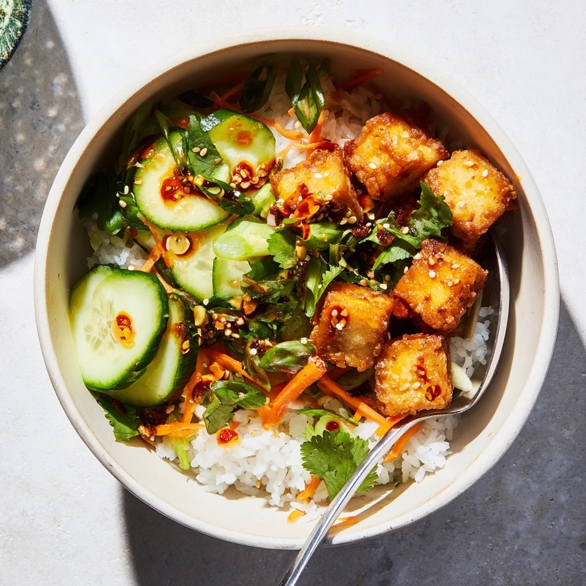 Golden crispy tofu cubes atop fluffy jasmine rice drizzled with spicy garlic chili oil and fresh garnishes